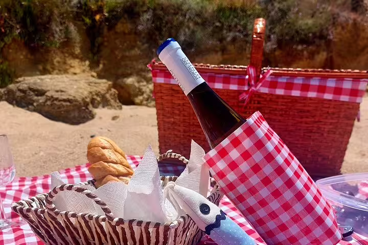 Beach picnic setup with wine and bread on a red checkered blanket, perfect for a private 4X4 Jeep tour in Arrábida, Sesimbra-Lisbon.