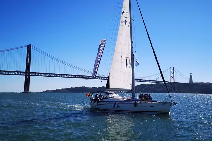 Sailing yacht on a private Lisbon cruise near the 25 de Abril Bridge and Cristo Rei monument on Tagus River