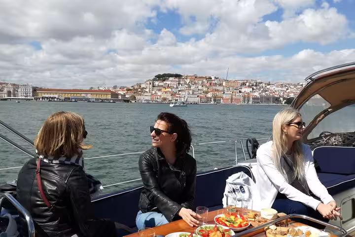 Guests enjoy snacks on a private Lisbon sailing yacht cruise on the Tagus River with city skyline views