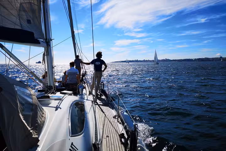 Guests relax on a private Lisbon sailing yacht cruise on the Tagus River under clear blue skies