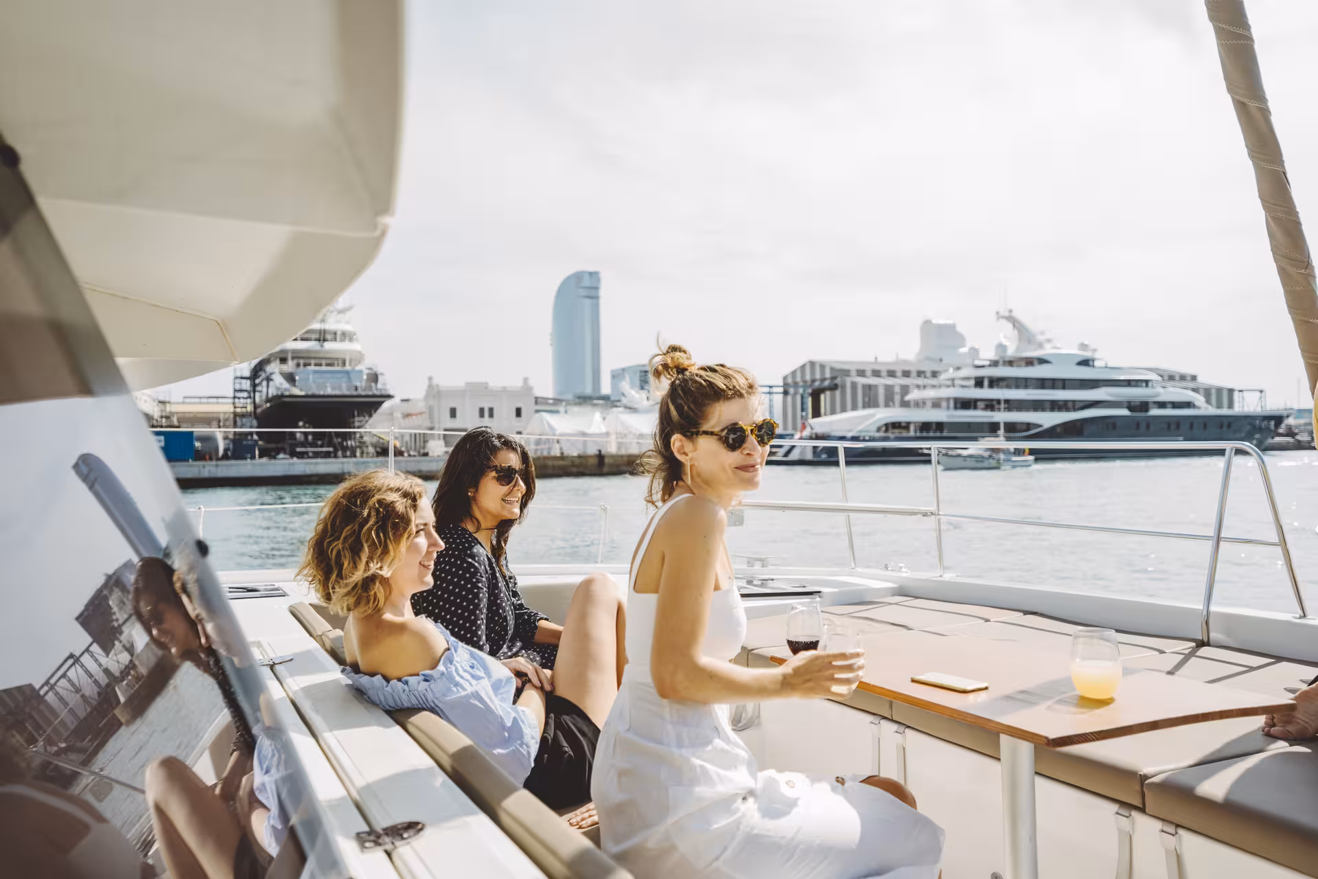 Guests relaxing with drinks on Bali 4.1 private luxury catamaran in Barcelona Port Vell with skyline views