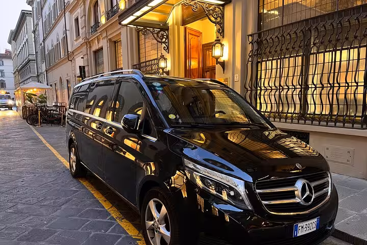 Elegant black Mercedes van ready for private airport transfer, parked outside a stylish building in Florence.