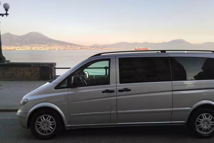 Comfortable private minivan parked on the Naples seafront with Mount Vesuvius in the background for a half-day guided tour