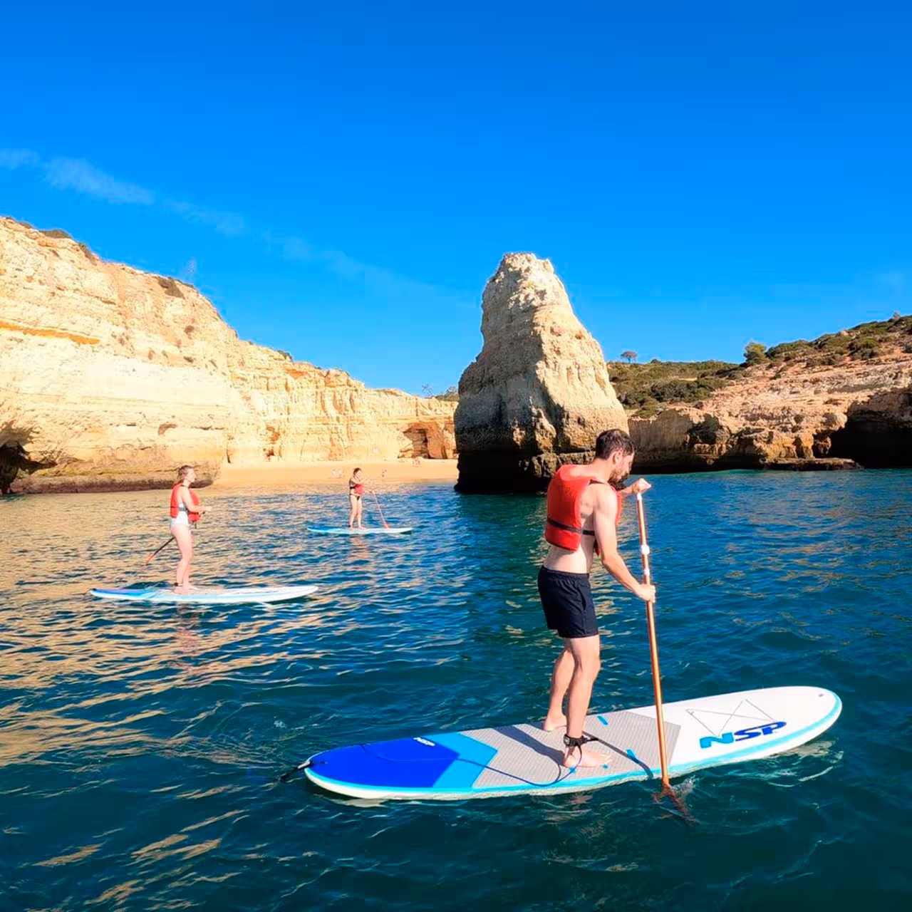 Group enjoying stand-up paddleboarding lessons near stunning coastal cliffs on clear blue water.