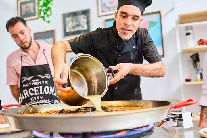 Chef demonstrates paella cooking techniques during private class in Barcelona kitchen, highlighting fresh market ingredients.