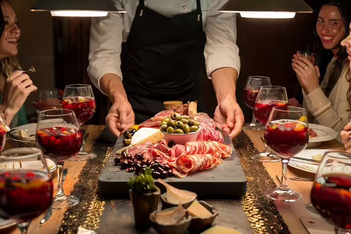 Chef presents a charcuterie board to guests enjoying sangria during a private paella cooking class and market visit experience.