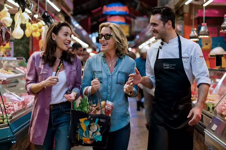 A personal chef guides two women through a vibrant market, preparing for an immersive private paella cooking class experience.