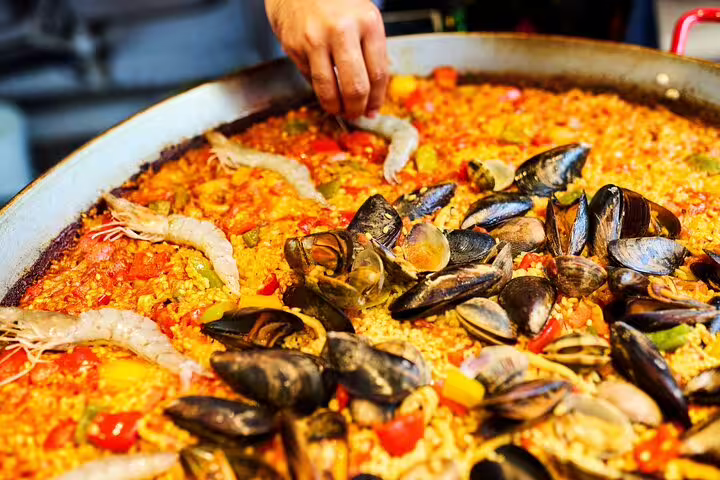 A chef's hand adds fresh seafood to a vibrant paella, highlighting a private cooking class experience with market-fresh ingredients.
