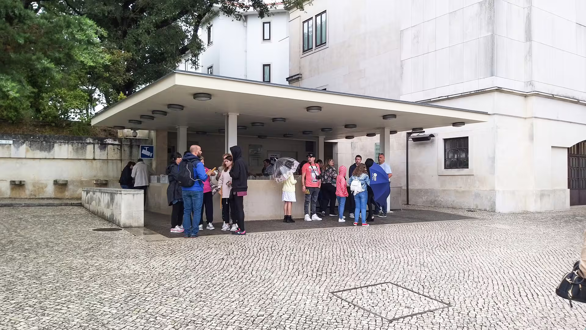 Group of tourists gathers under a modern shelter, preparing for a customizable private tour from Porto to Lisbon.