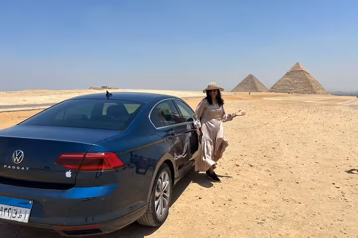 A tourist poses beside a car with the pyramids in the background, highlighting a stop on the Private 3 Days tour.