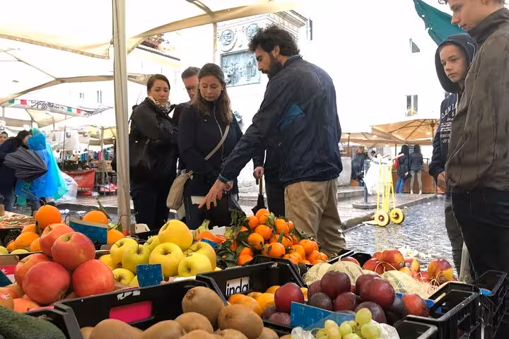 Tour group exploring fresh produce at a vibrant Roman market during the Private Roman Vegetarian Food Tour.