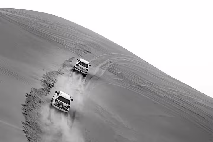 Thrilling desert adventure with two 4x4 vehicles navigating steep sand dunes on a private safari tour.