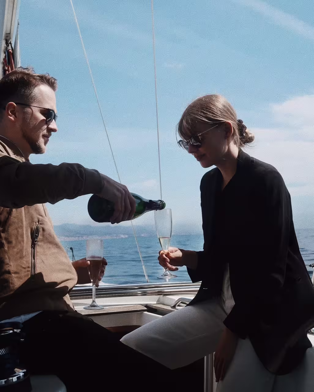 Couple enjoys a luxurious private sailing experience in Barcelona, sipping champagne on an elegant boat against a sunny seascape.