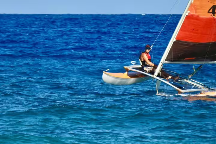 Man enjoying a full-day private sailing cruise on a vibrant catamaran in crystal-clear blue waters under a sunny sky.