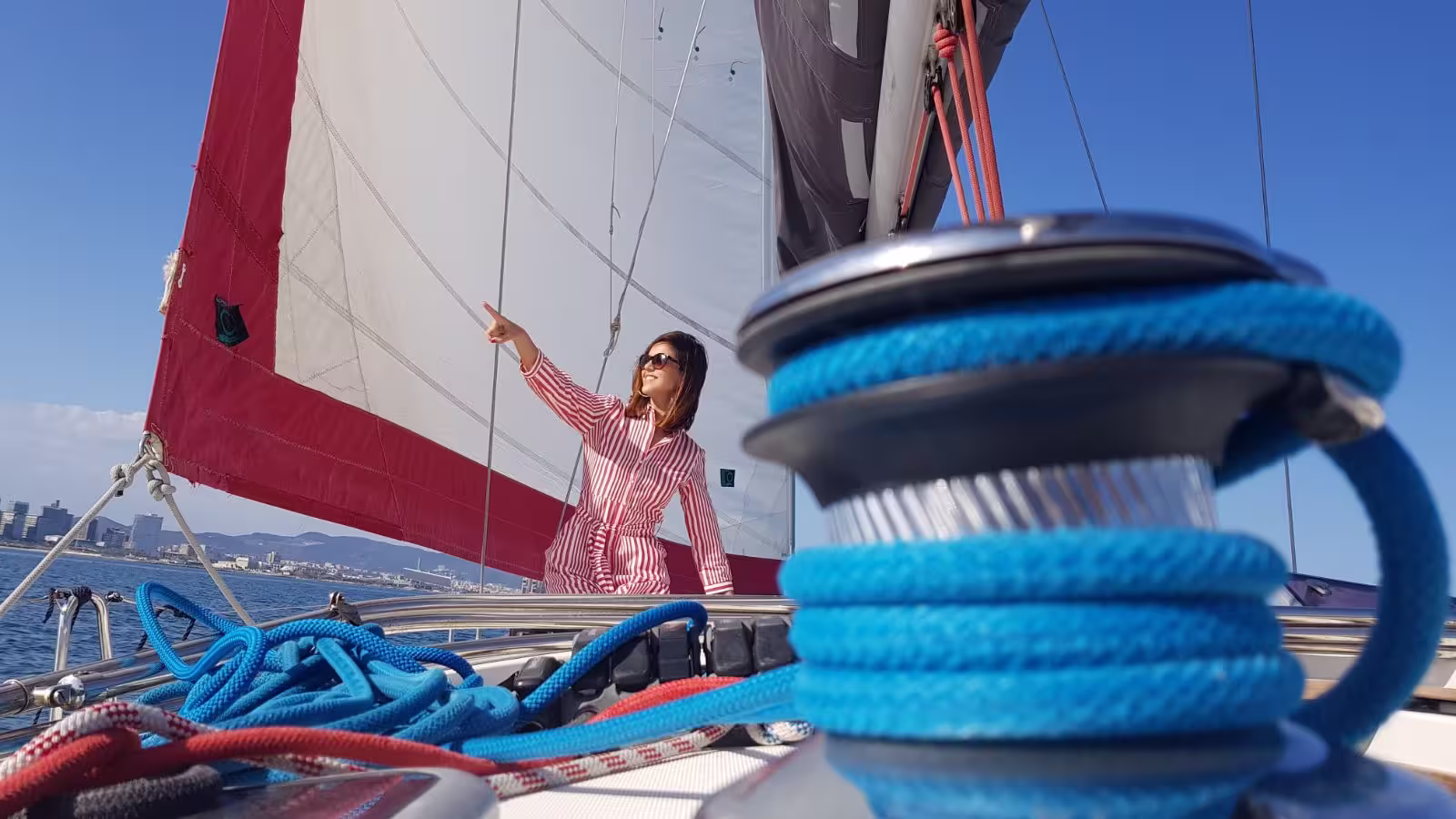 Woman enjoying a private 3-hour sailing experience in Barcelona with vibrant sails and a city skyline in the background.