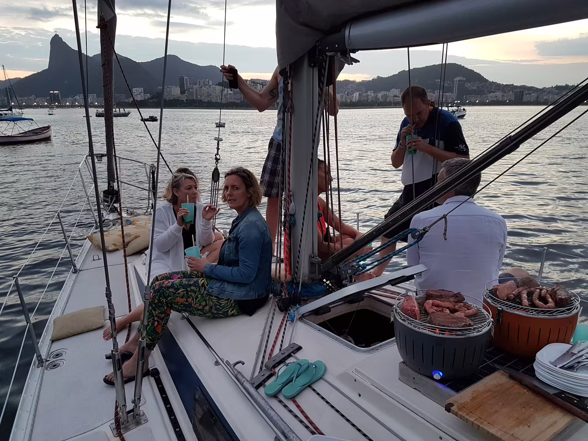 Group enjoying a BBQ on a private sailing tour with scenic views of the city and mountains at sunset.