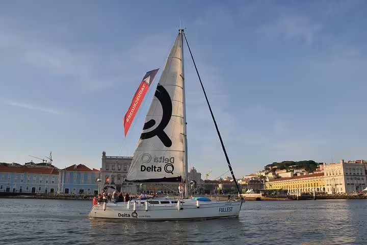 Sailboat with Delta Q branding glides along Lisbon's waterfront on a sunny day during a private sailing tour.
