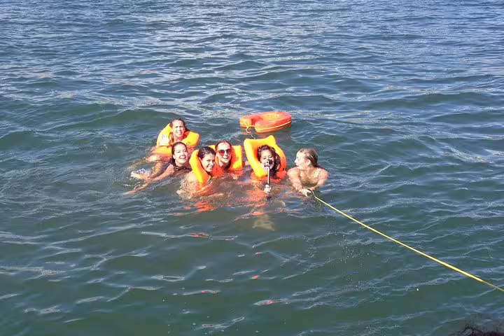 Group of friends swimming with life jackets during a private sailing trip to Oeiras beach.