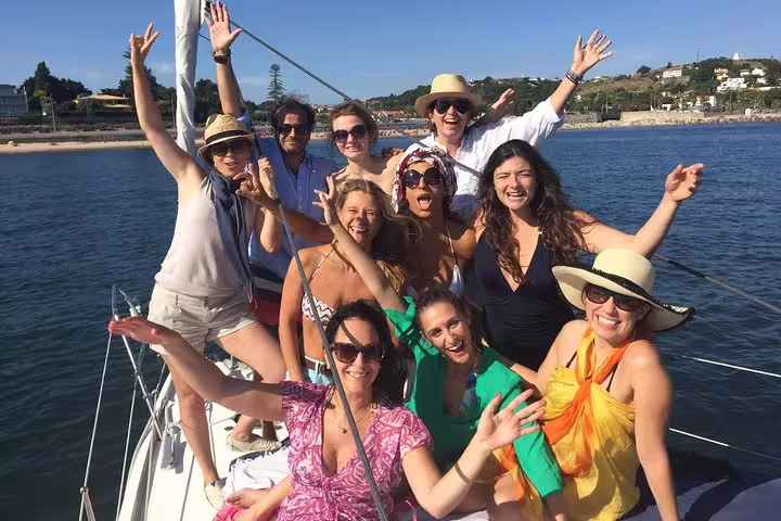 Happy group of tourists enjoying a sunny day on a private sailboat near Oeiras beach.