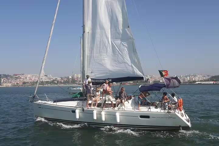 People sailing on a yacht with full sails during a private tour near Oeiras beach.