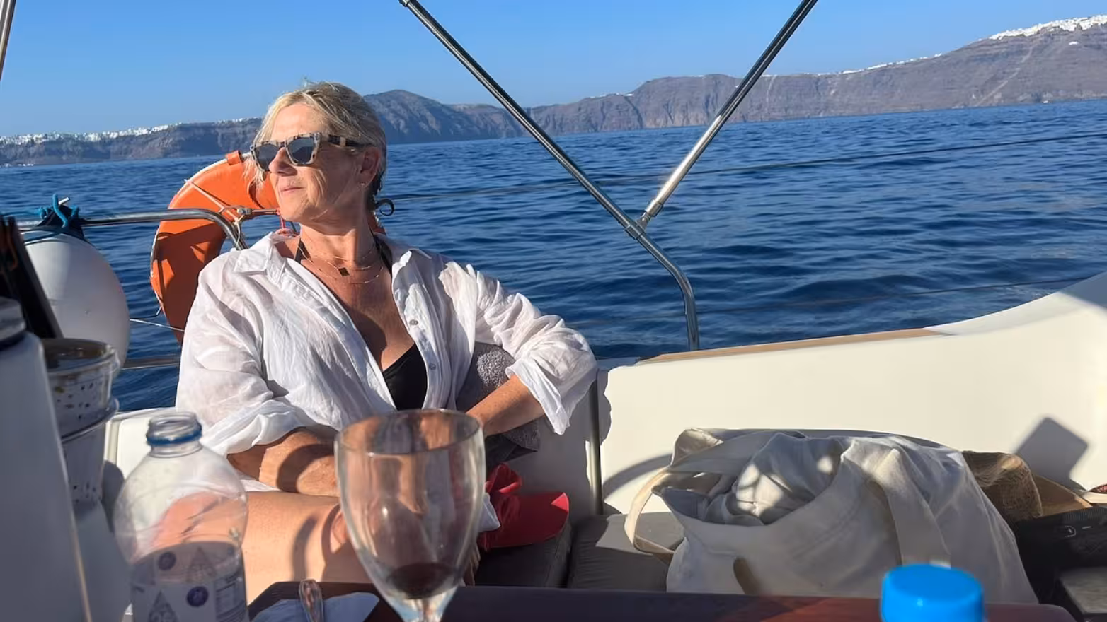Guest relaxing on a private Santorini caldera sailing cruise, enjoying Aegean Sea views and onboard drinks