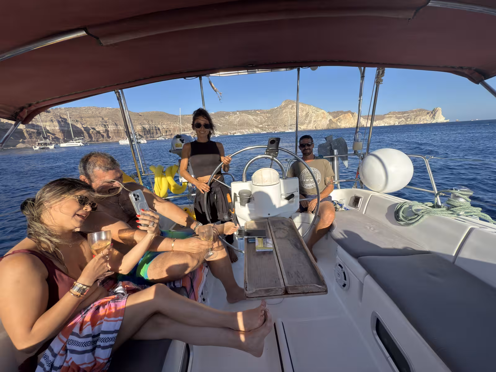 Guests relax on a private Santorini sunset sailing cruise, sipping wine with caldera cliffs in view