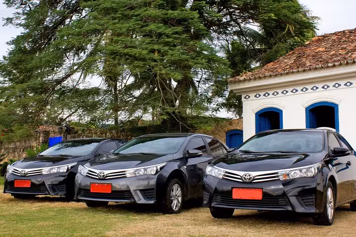 Fleet of private shuttle cars ready in Rio de Janeiro for transport service to Buzios, parked near a picturesque building.