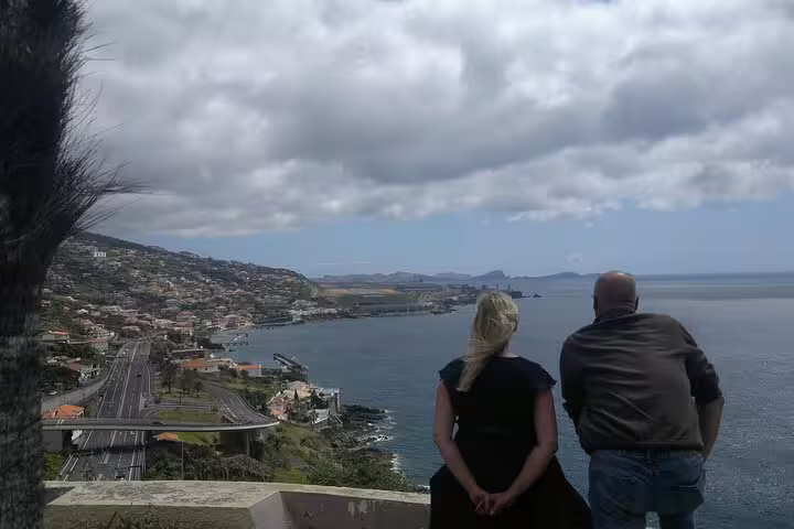 Two people enjoy a breathtaking coastal view of Funchal from a scenic overlook, perfect for a sidecar adventure tour.