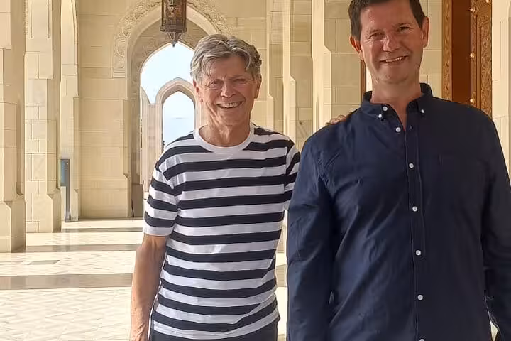 Two travelers enjoy a private sightseeing tour at Muscat’s grand mosque, posing under ornate arches and marble walkways