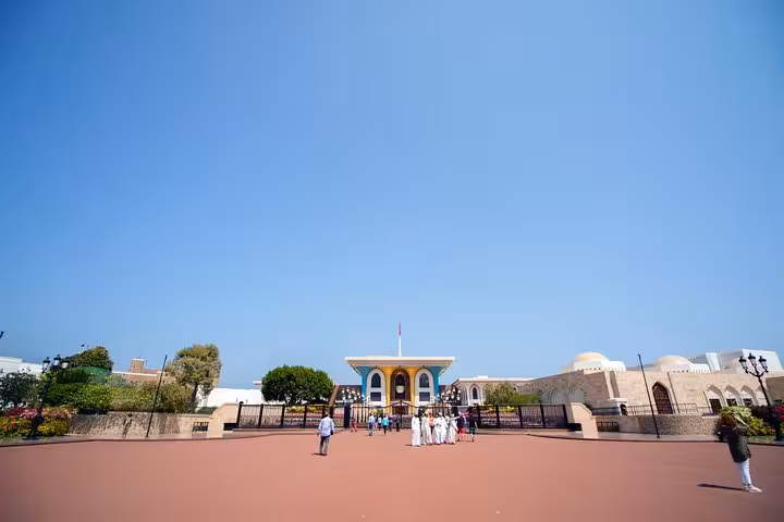 Visitors exploring the grand ceremonial palace area in Muscat, Oman, under a clear blue sky on a private sightseeing tour