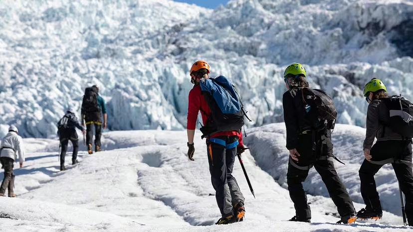 Group of hikers with helmets and crampons trekking across an Iceland glacier with ice formations behind