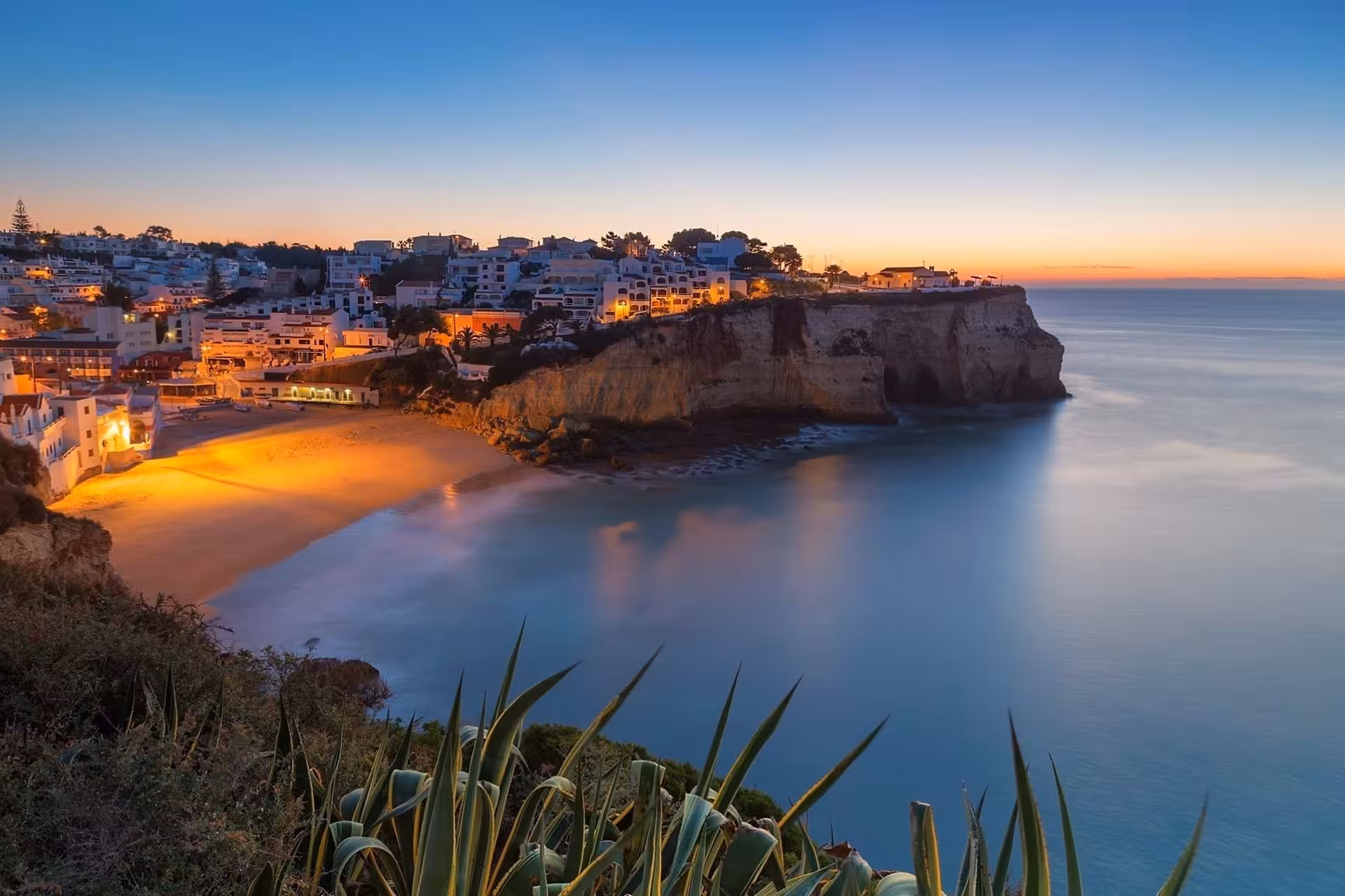 Twilight view of Algarve coastal village and illuminated cliff beach admired from a private sunset boat tour