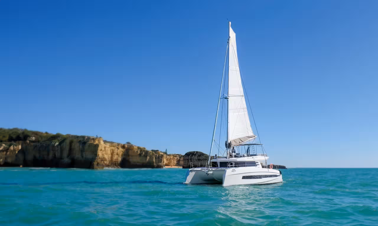 White sailing catamaran anchored near golden Algarve cliffs on a private Vilamoura sunset cruise tour
