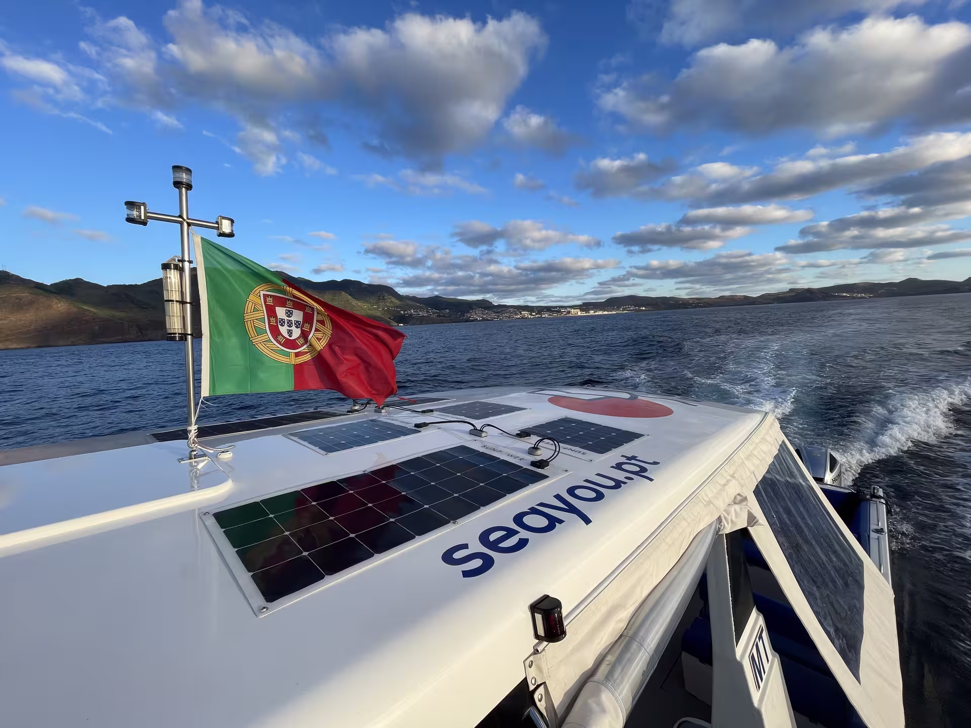 Boat with Portuguese flag cruising under a blue sky, offering a serene private sunset experience on the open sea.