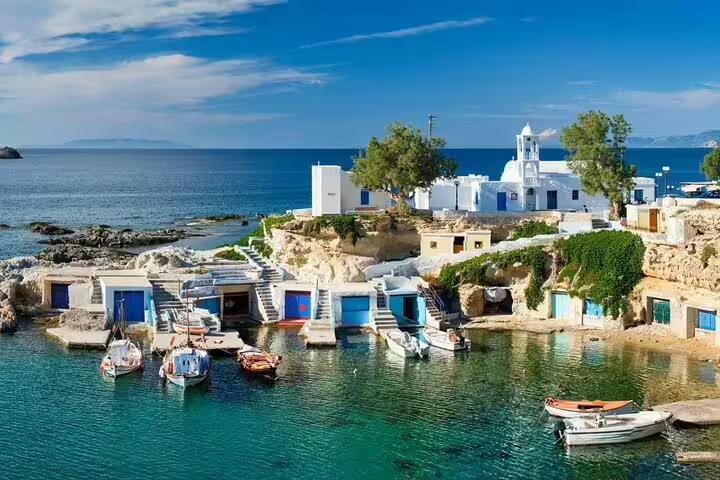 Scenic view of motorboats docked by the picturesque whitewashed village of Milos, Greece, ideal for a private sunset tour.