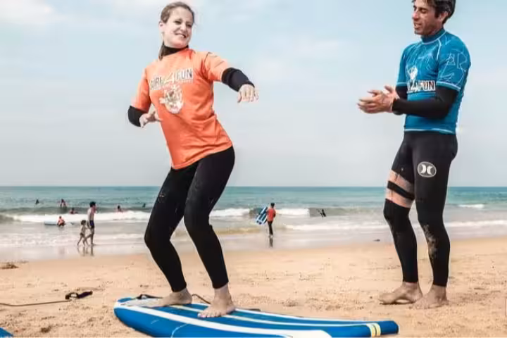 Smiling student practicing surf stance on board with expert instructor during private surf lesson at Albufeira Algarve