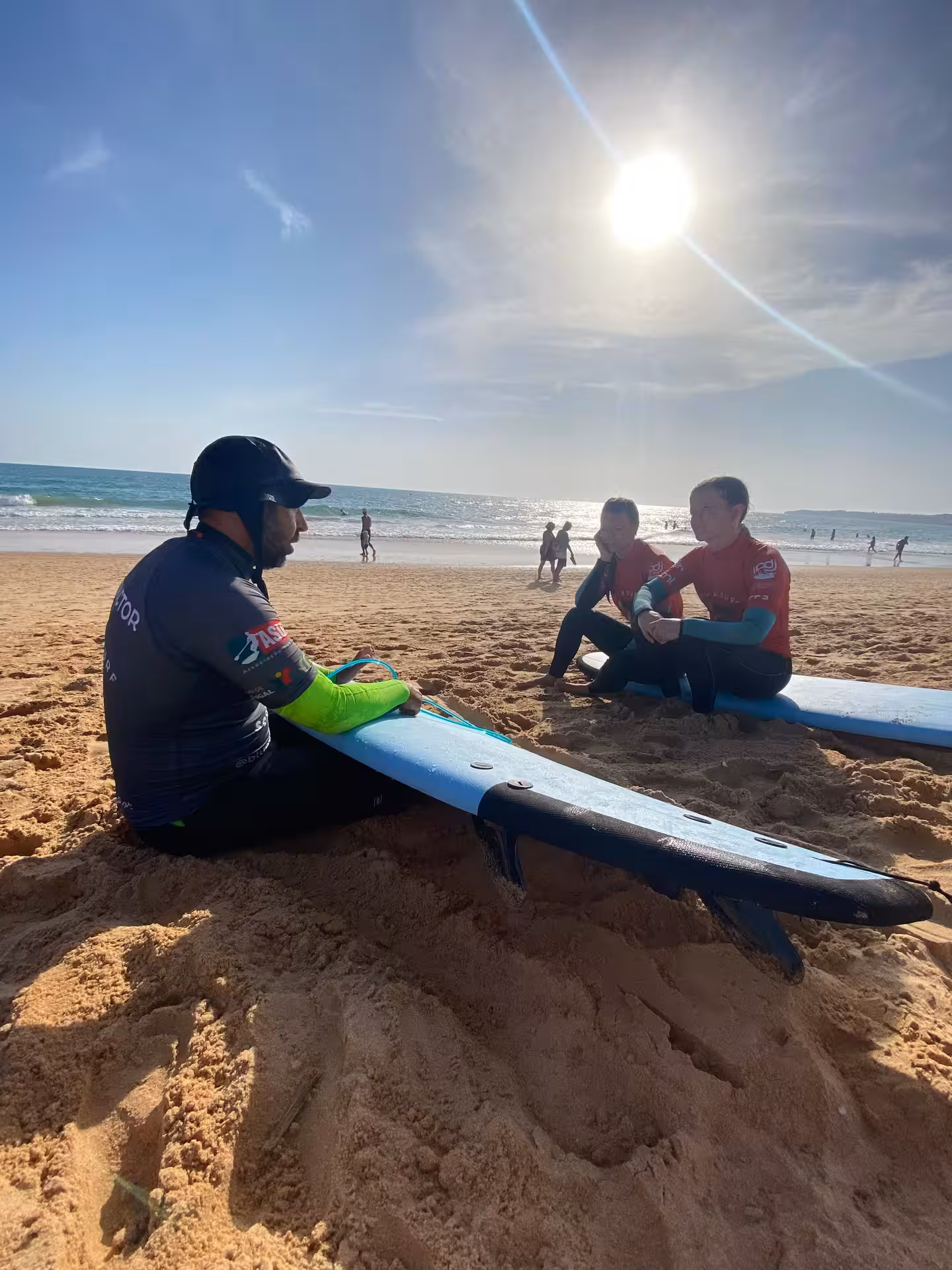 Surf coach explaining paddle and pop-up techniques on the sand to two beginners before their private small-group lesson