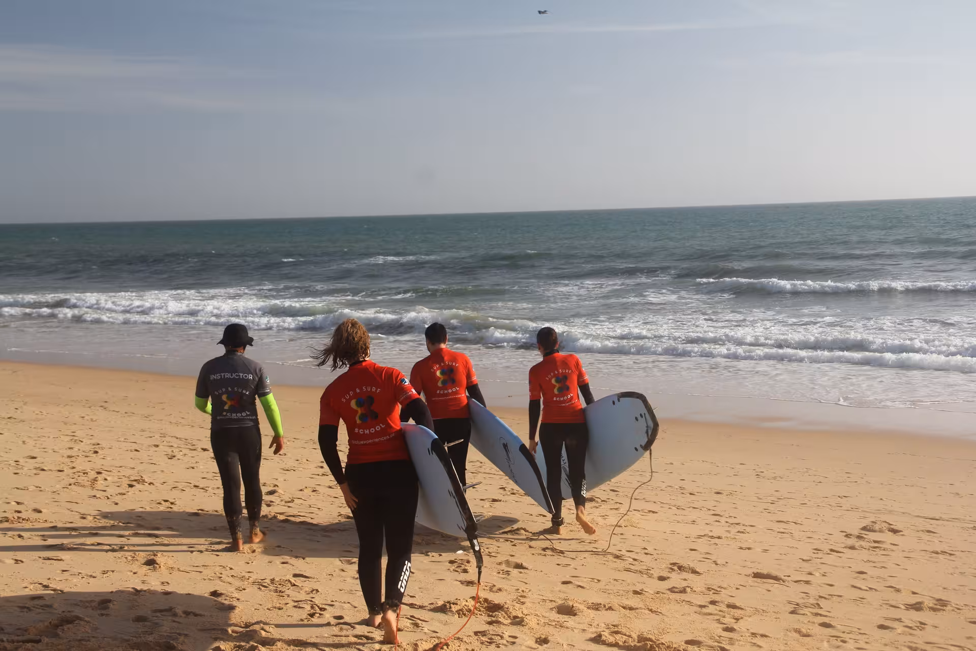 Surf instructor leading a small group of students carrying boards along a sandy beach to start their private lesson