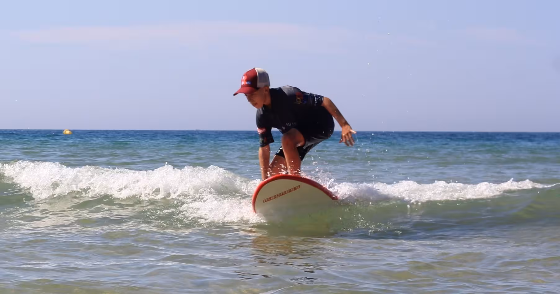 Young surfer standing up on a small wave in a private surf lesson, practicing pop-up technique in clear, waist-deep water