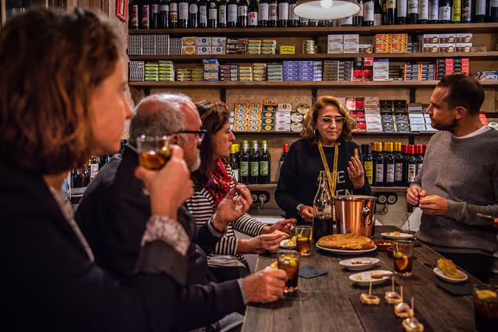 Group enjoying a private tapas and wine tour in a cozy Spanish bodega with various wines and tapas on display.