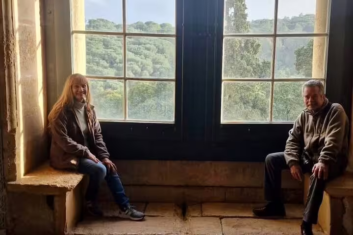 Visitors enjoy a peaceful moment by a large window overlooking lush greenery on a private full-day tour from Lisbon to Tomar and Coimbra.