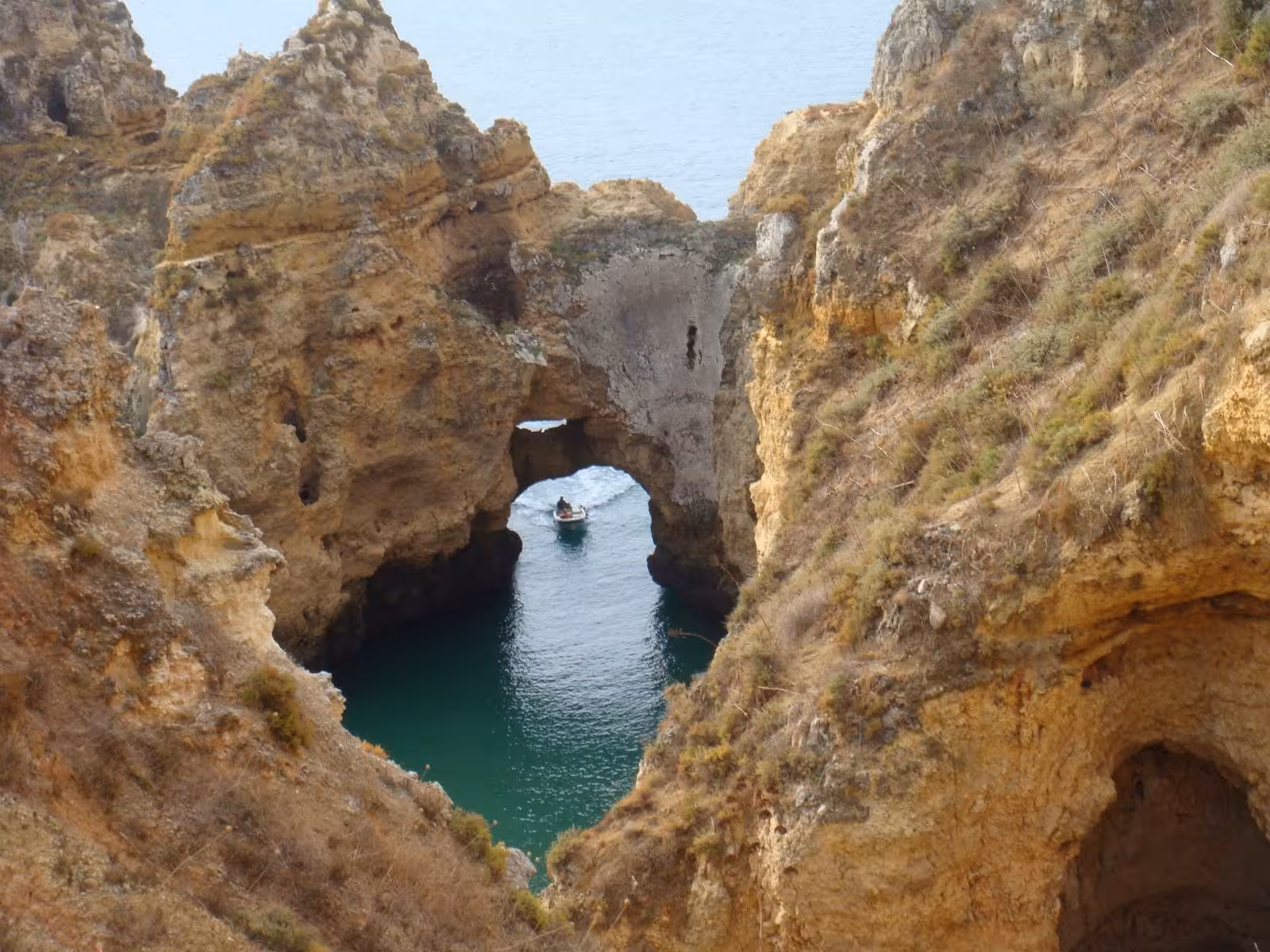 Small boat passing through Ponta da Piedade rock arch and grotto near Lagos on Algarve sunset cruise