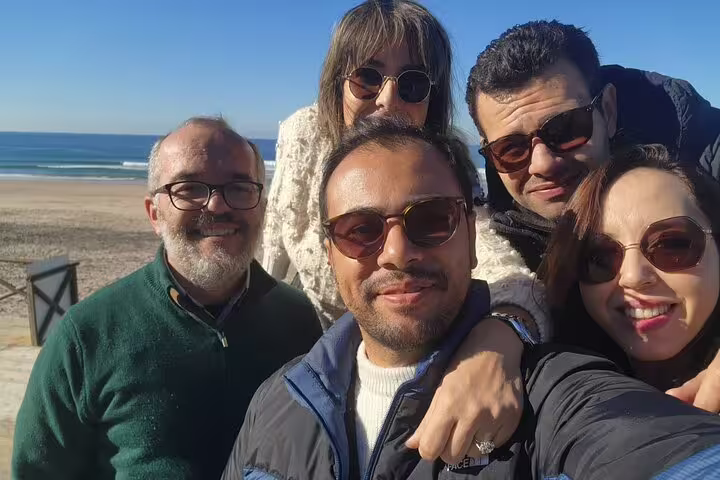 A group of tourists enjoying a sunny day at a coastal viewpoint during a private tour from Lisbon to Sintra's Pena and Regaleira Palaces.