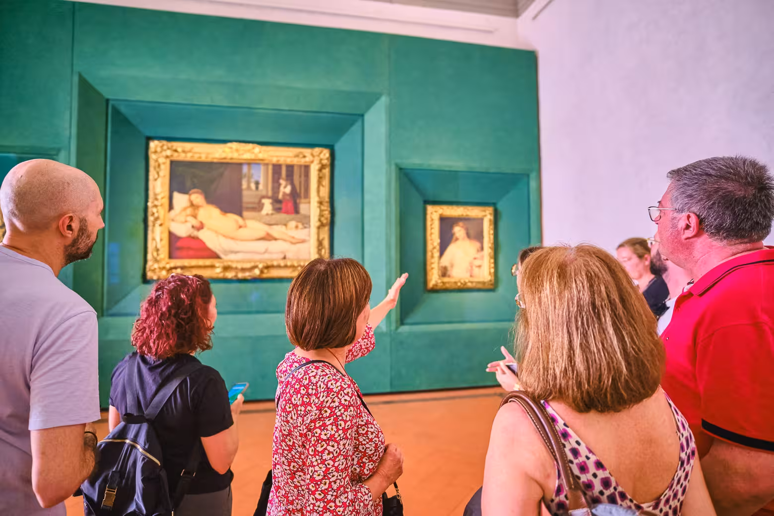 A guide discusses famous paintings with a group during a private tour in the Uffizi Gallery's vibrant exhibition room.