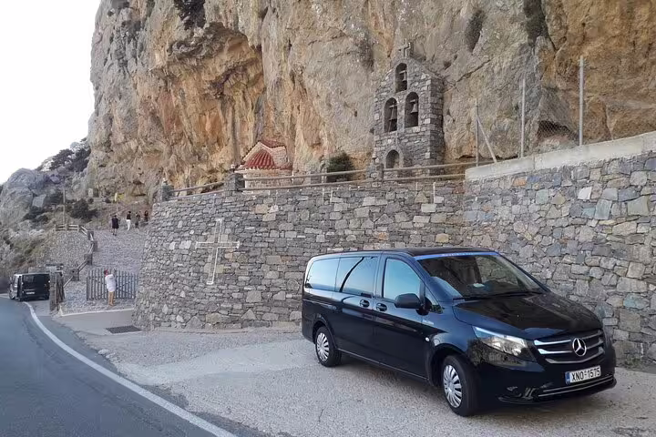Private tour van parked by a historic stone chapel along Crete's scenic south coast road.