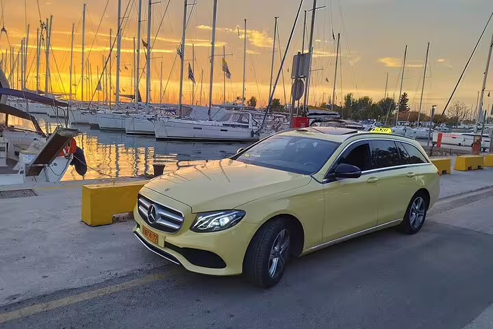 Private taxi transfer from Athens Airport to Piraeus Port, luxury sedan by marina at sunset