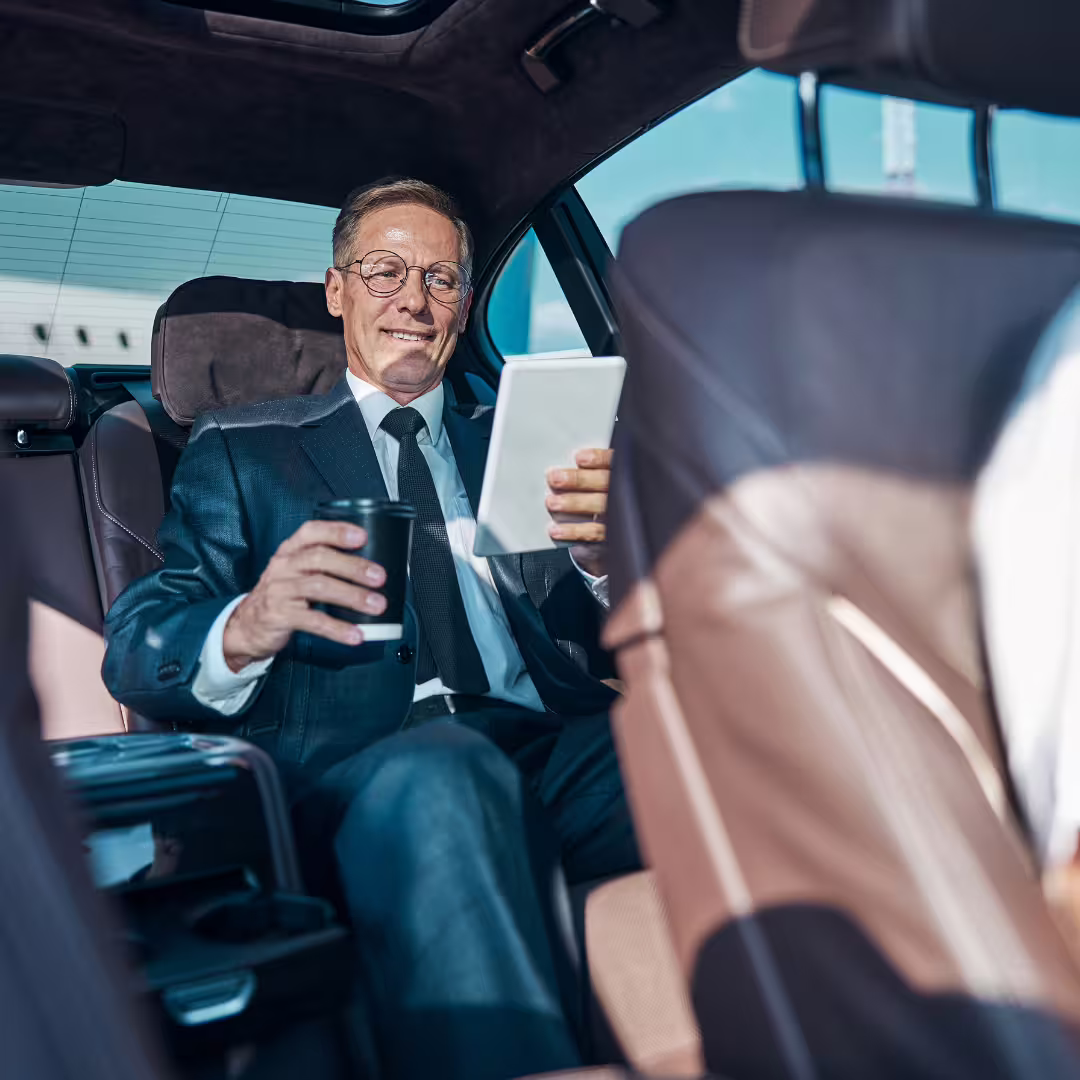 Business traveler relaxing with tablet in executive car during private transfer between Alberi del Paradiso Cefalù and Palermo airport