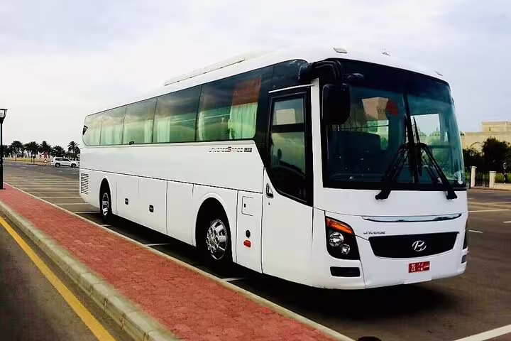 Spacious white tour bus ready for private transfer from Dubai to Muscat, offering comfort and convenience.