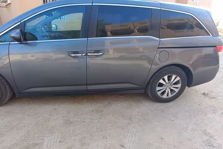 Modern grey minivan parked on sandy road ready for private transfer service between Muscat and Nizwa in Oman
