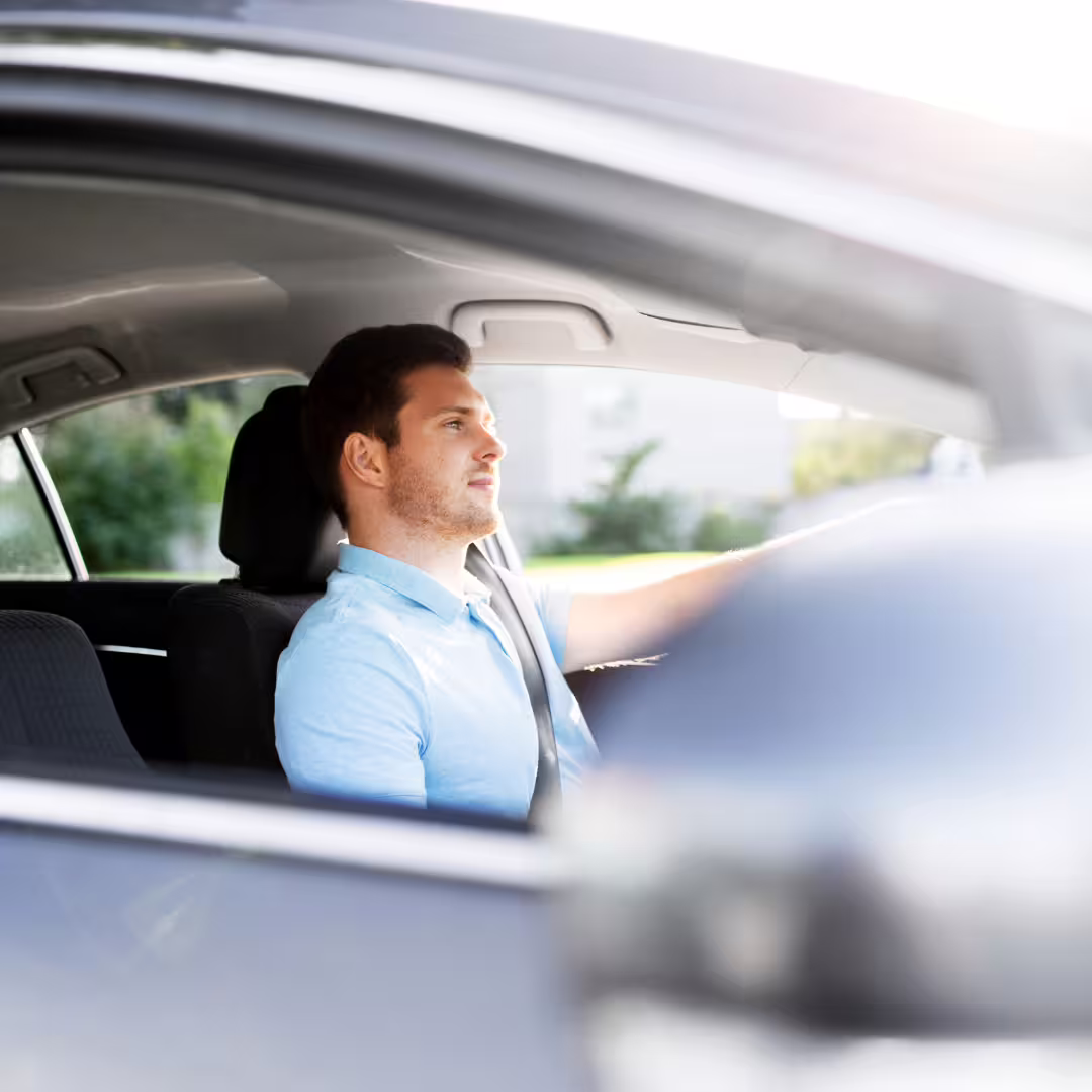 Male driver in casual shirt steering car on sunny day, providing comfortable private transfer from Naples airport